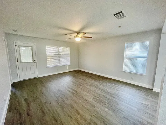an empty room with wooden floor chandelier fan and windows