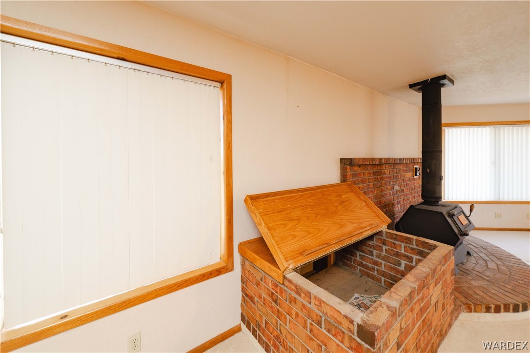 2100 East Valley View Road Kingman, AZ 86409 - Photo 16 of 53 Brick hearth with integrated wood storage featuring a wood-burning stove, brick flooring, and wood-trimmed windows