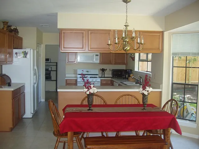 a kitchen with stainless steel appliances granite countertop a dining table chairs refrigerator and sink