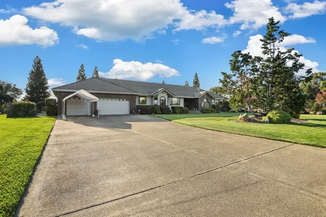 a view of a white house with a big yard plants and large trees