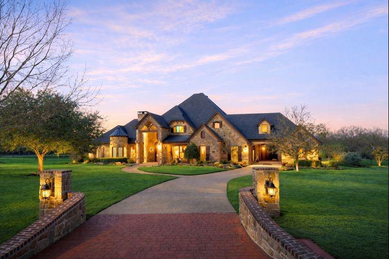 French country home featuring stone siding, a lawn, decorative driveway, and a chimney