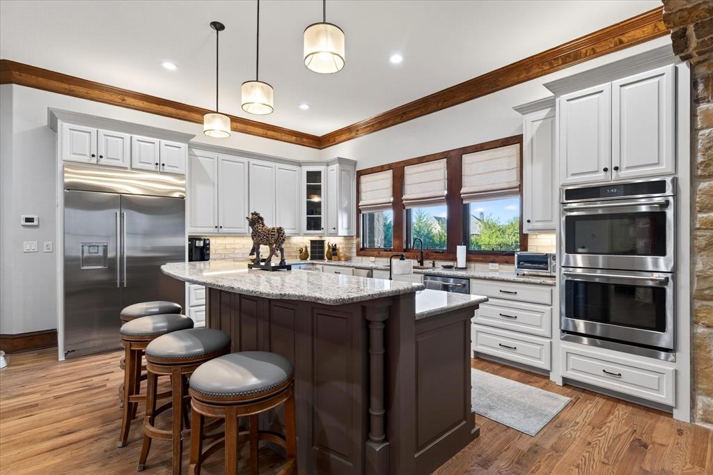 1625 Timber Ridge Trail Cross Roads, TX 76227 - Photo 23 of 40 Kitchen featuring decorative light fixtures, appliances with stainless steel finishes, glass insert cabinets, a center island, and light stone counters