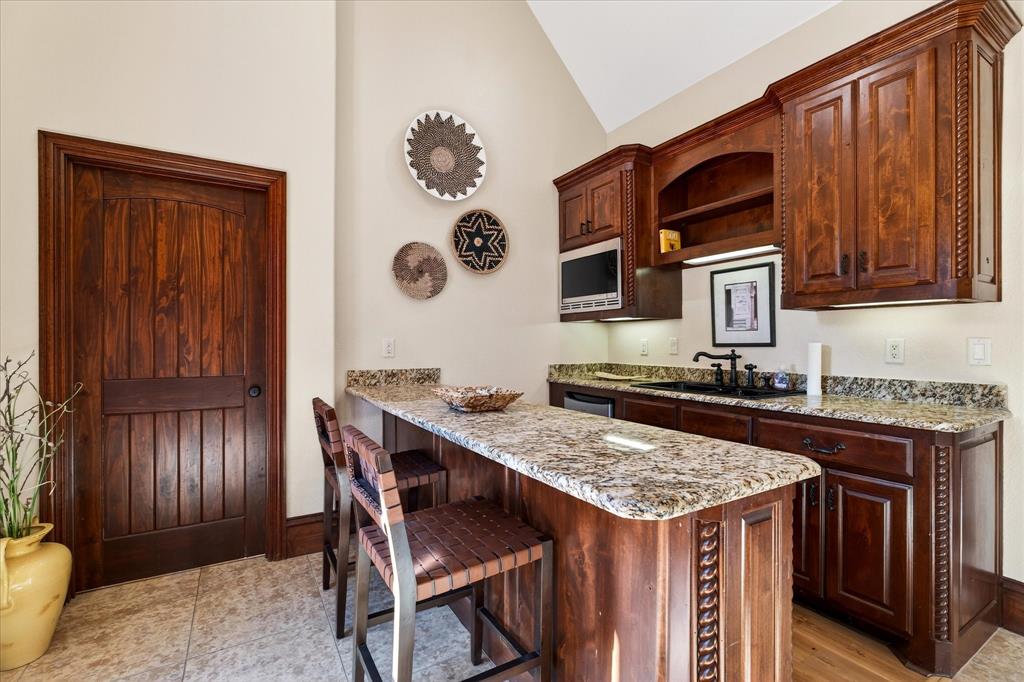 1625 Timber Ridge Trail Cross Roads, TX 76227 - Photo 32 of 40 Kitchen with a breakfast bar, a peninsula, light stone countertops, open shelves, and dark brown cabinetry
