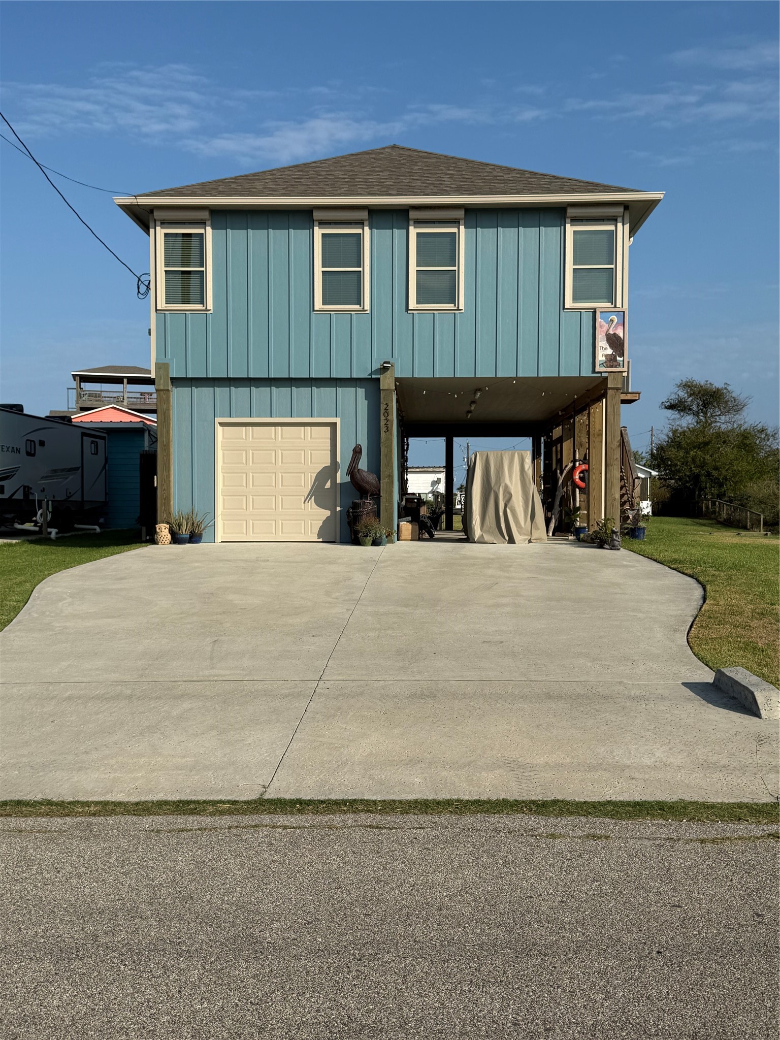 2023 County Road 201 Sargent, TX 77414 - Photo 11 of 45 This elevated two-story home features a blue facade with a single garage and a spacious driveway. The open area underneath offers additional covered parking or storage space.
