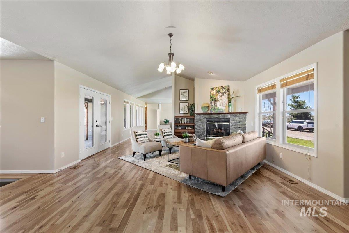 147 East Indian Crk Road Boise, ID 83716 - Photo 8 of 43 Vaulted ceiling living area featuring wood-finish flooring, a stone-clad fireplace with a wood mantle, and white frame windows with integrated blinds