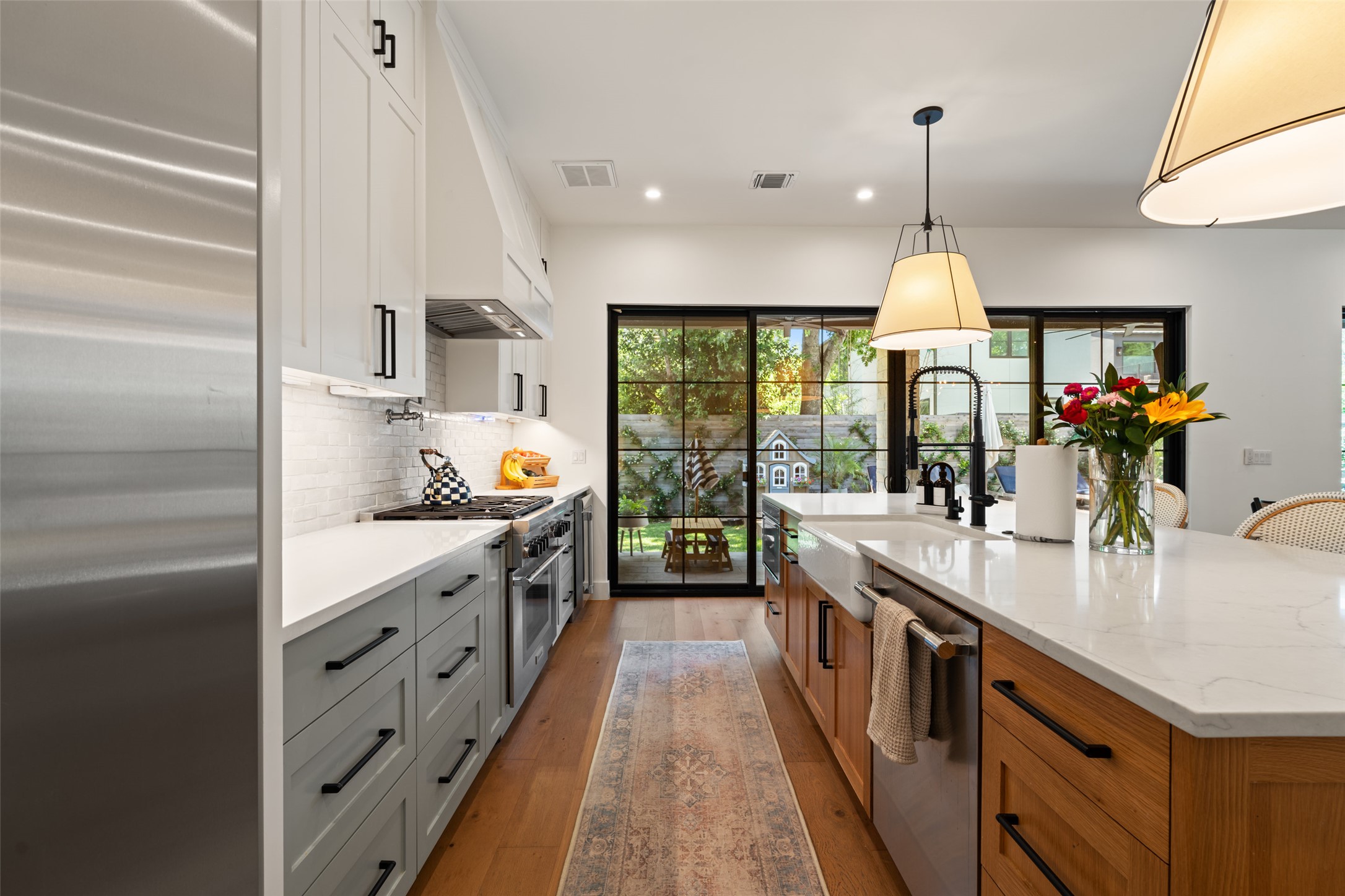 2107 Peach Tree Street Austin, TX 78704 - Photo 11 of 40 Kitchen featuring appliances with stainless steel finishes, a sink, decorative backsplash, light wood finished floors, and a kitchen island with sink