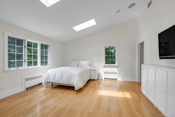 a spacious bedroom with a bed and a flat tv screen on dresser