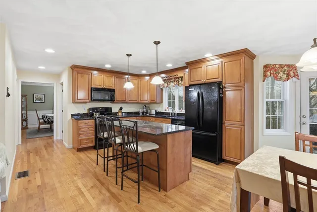 a kitchen with stainless steel appliances kitchen island granite countertop a refrigerator a stove a sink a dining table and chairs with wooden floor