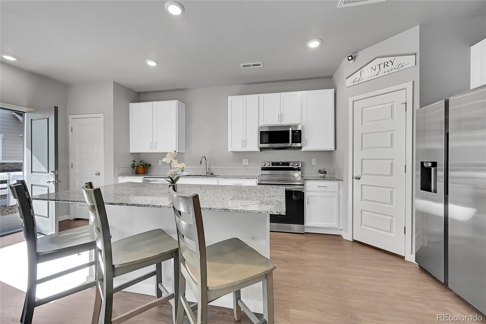 1353 Reynolds Street, Unit 3C Fort Lupton, CO 80621 - Photo 10 of 31 a kitchen with white cabinets and stainless steel appliances
