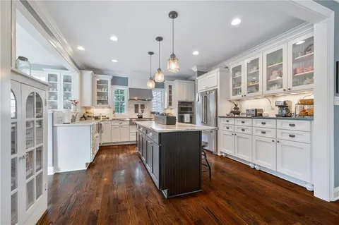 a kitchen with stainless steel appliances kitchen island granite countertop a refrigerator a oven a sink and white cabinets with wooden floor