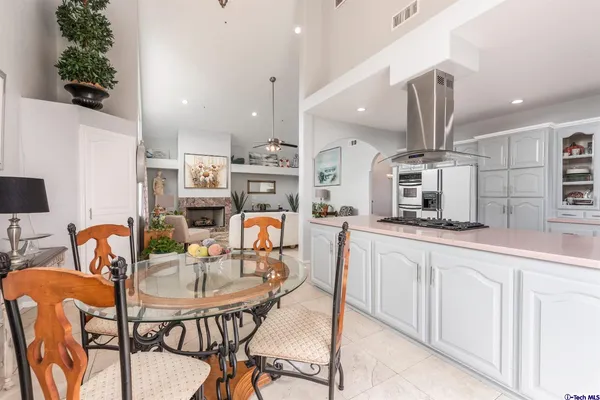 a kitchen with stainless steel appliances kitchen island granite countertop a dining table chairs sink and white cabinets