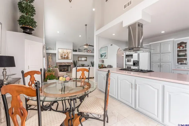 a kitchen with stainless steel appliances kitchen island granite countertop a dining table chairs sink and white cabinets