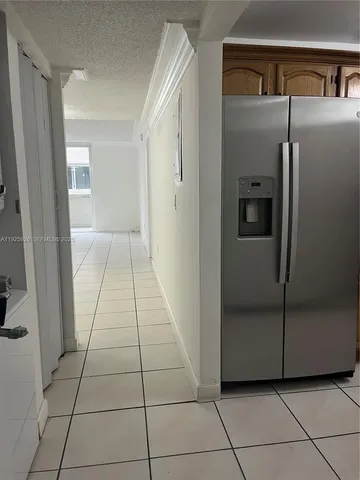 a view of a refrigerator in kitchen and an empty room in wooden floor