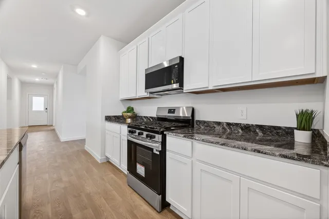 a kitchen with stainless steel appliances granite countertop grey cabinets a stove a sink and a microwave