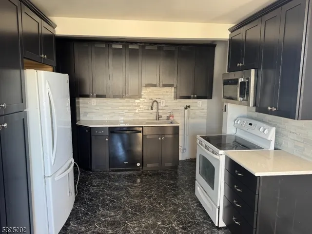 a kitchen with stainless steel appliances kitchen island granite countertop a refrigerator a stove and a sink with wooden cabinets