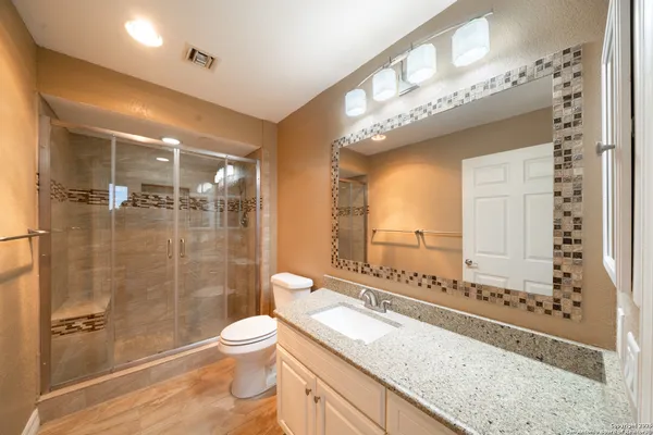 a bathroom with a granite countertop sink a toilet a mirror and shower