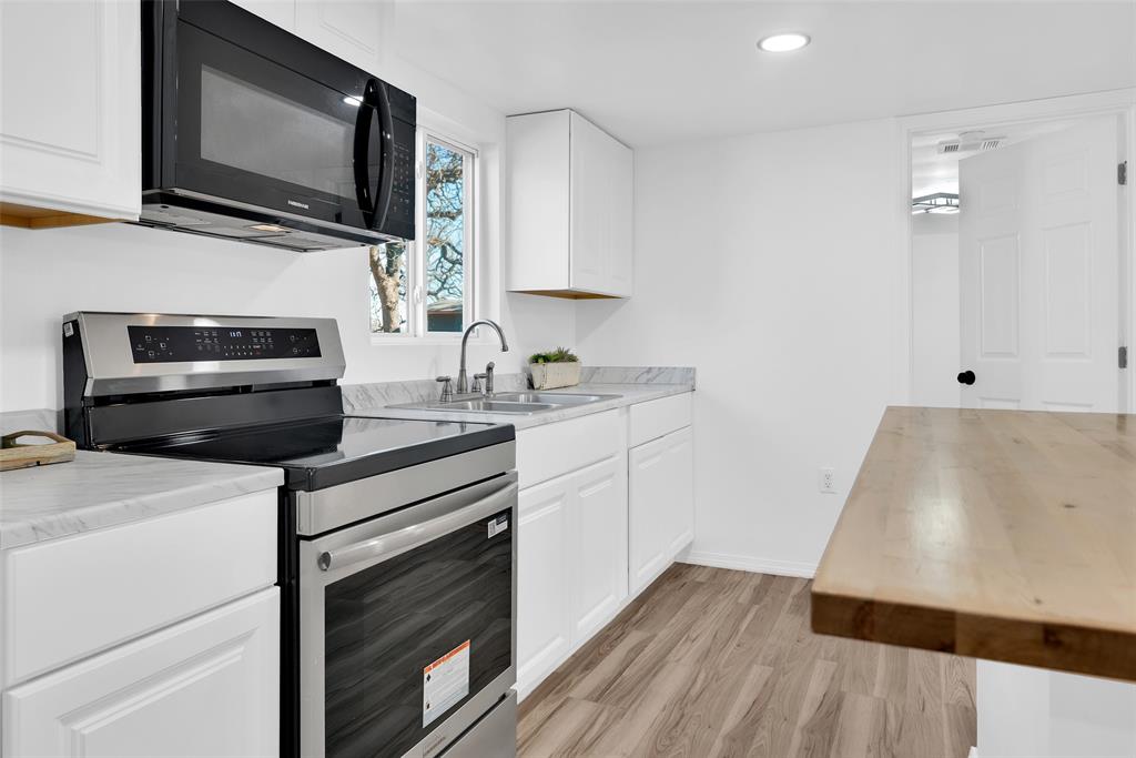 909 East Sears Street Denison, TX 75021 - Photo 6 of 24 Kitchen with stainless steel range with electric cooktop, black microwave, wood counters, white cabinets, and light wood-type flooring