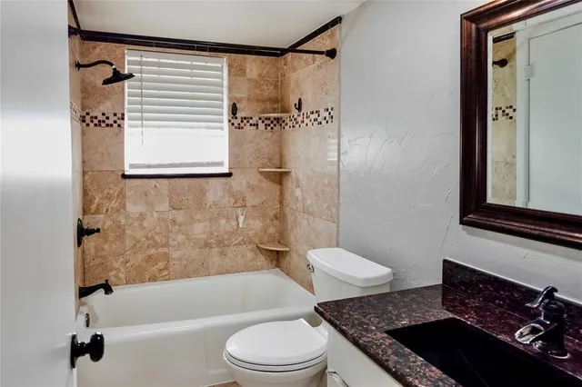 a bathroom with a granite countertop bathtub sink vanity mirror and toilet