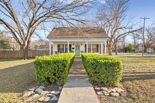 a view of a brick house with a big yard plants and large trees