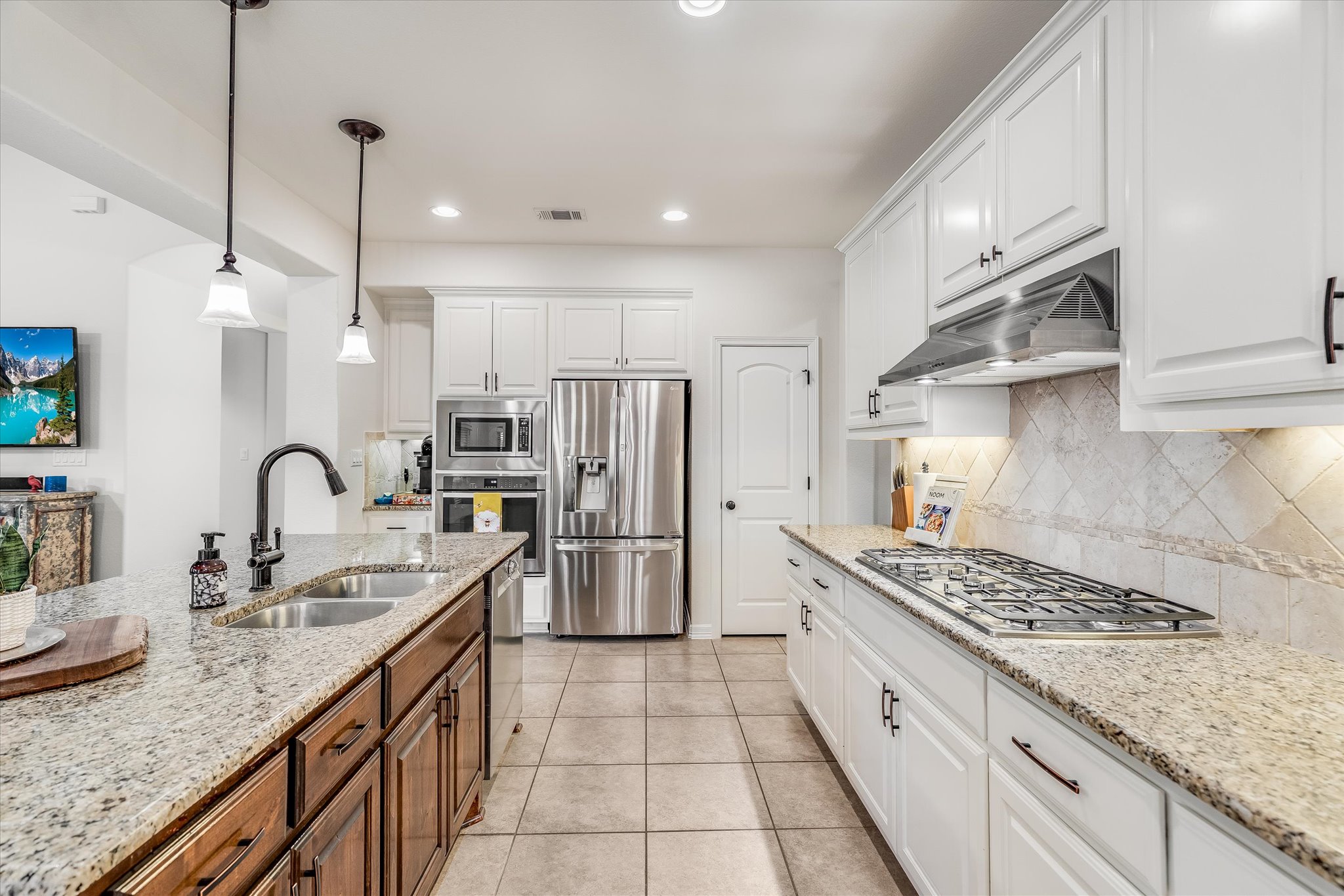 226 Galloway Lane Austin, TX 78737 - Photo 12 of 30 Kitchen with stainless steel appliances, light stone counters, two tone cabinets, decorative light fixtures, and decorative backsplash