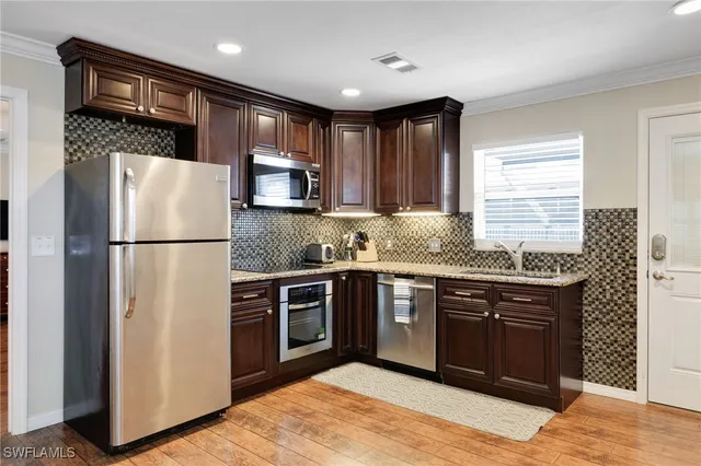 a kitchen with stainless steel appliances a stove a refrigerator a dining table and chairs with wooden floor