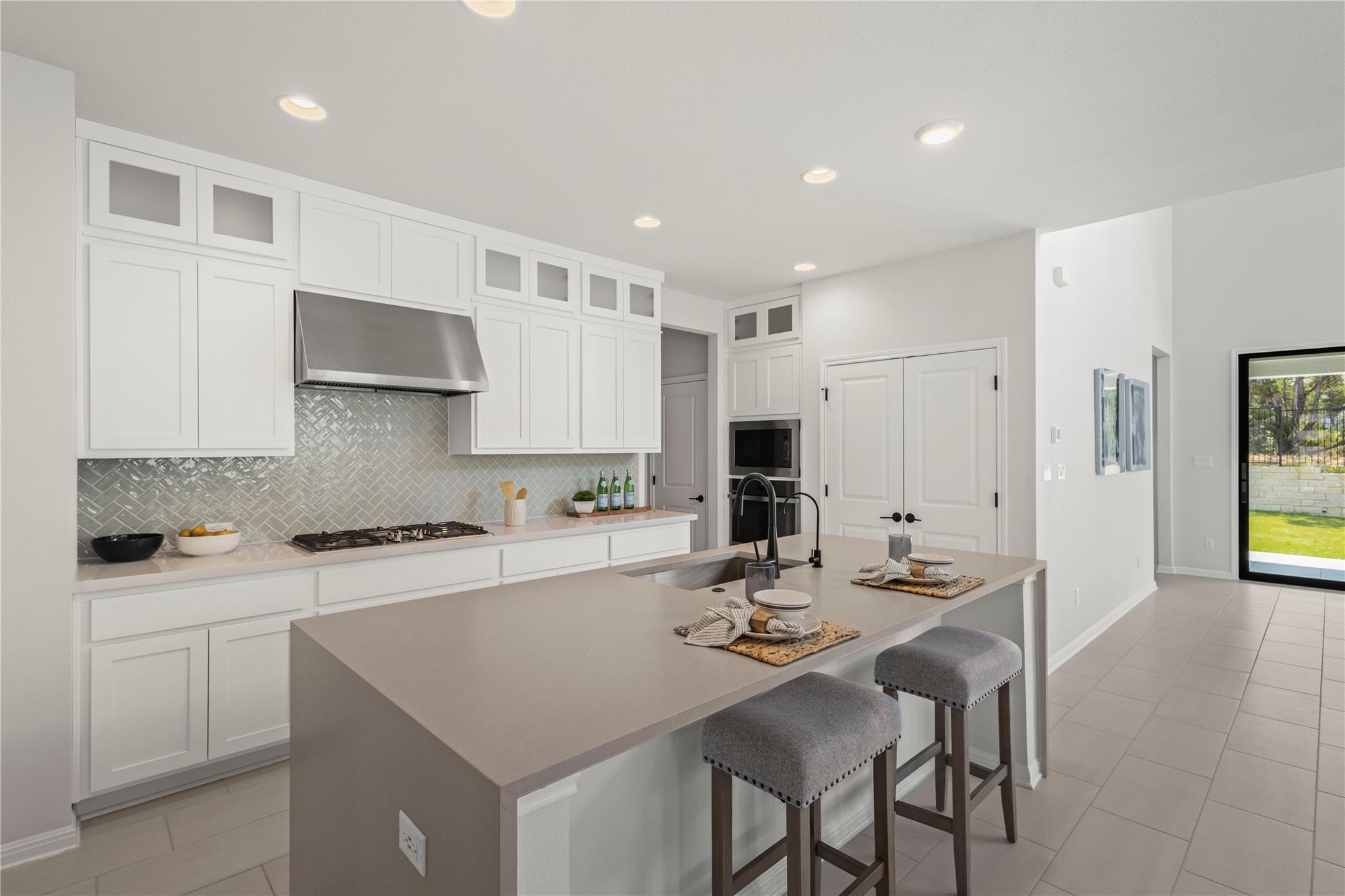 1128 Villa Rialto View Leander, TX 78641 - Photo 14 of 40 Kitchen with glass fronted cabinets, white cabinets, a kitchen bar, light stone countertops, and recessed lighting