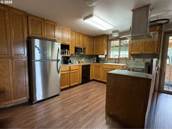 a kitchen with stainless steel appliances granite countertop a refrigerator a sink dishwasher a stove top oven a kitchen island and chairs with wooden floor