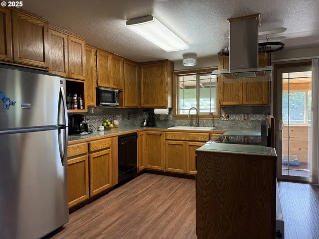 a kitchen with granite countertop wooden floors stainless steel appliances a sink and a window