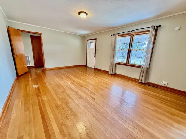 a view of an empty room with wooden floor and a window