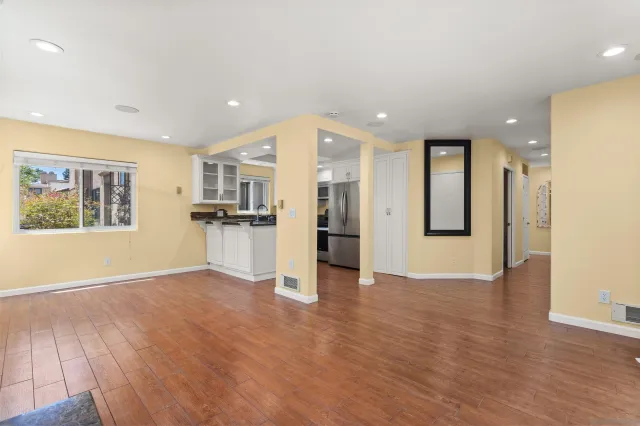 a view of an empty room with wooden floor and a kitchen