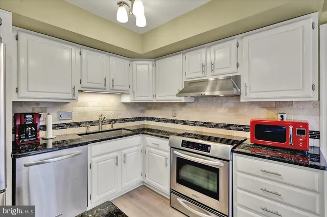 a kitchen with stainless steel appliances granite countertop a stove a sink and white cabinets