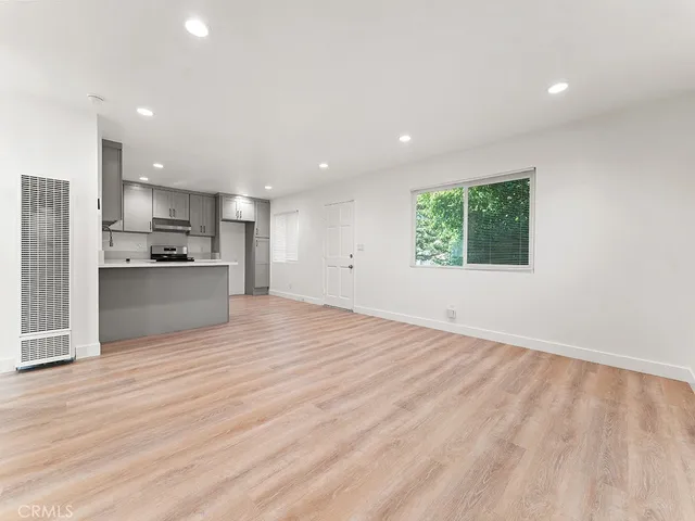an empty room with wooden floor and a kitchen