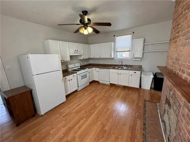 a kitchen with granite countertop a refrigerator a sink dishwasher a stove and white countertops with wooden floor