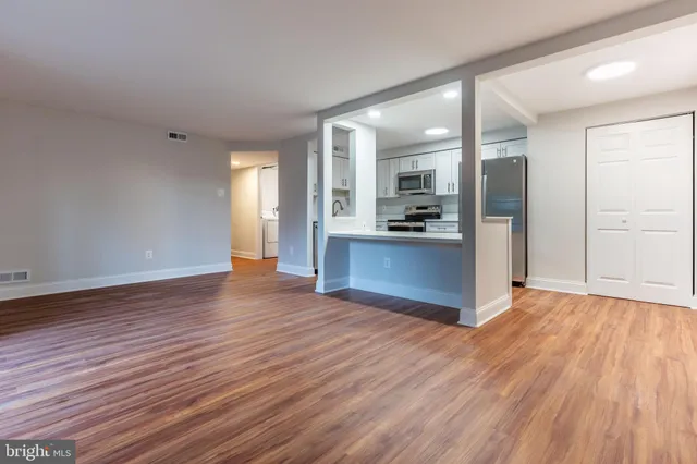 an empty room with wooden floor and kitchen view