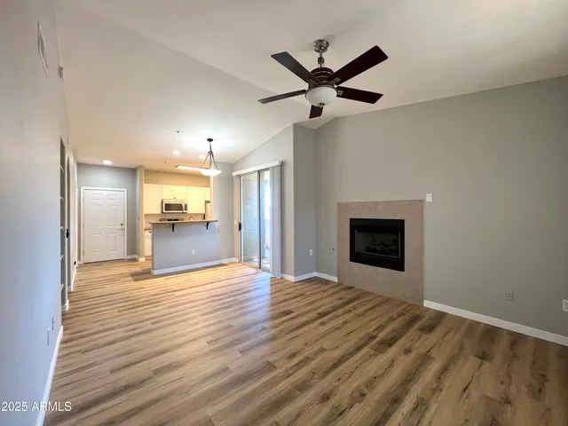 a view of a livingroom with a fireplace a ceiling fan and wooden floor