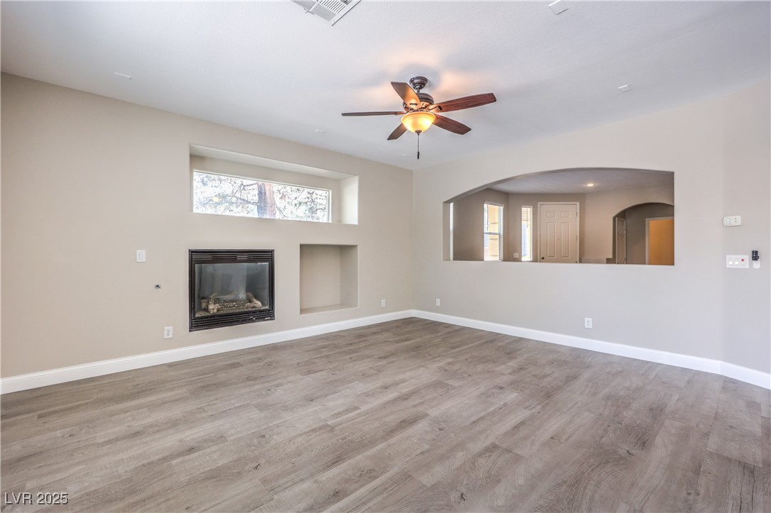 585 Foster Springs Road Las Vegas, NV 89148 - Photo 12 of 39 Unfurnished living room with healthy amount of natural light, ceiling fan, a glass covered fireplace, and wood finished floors