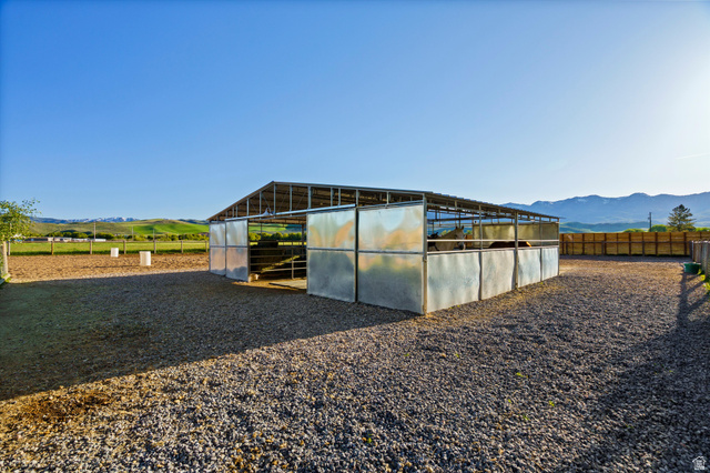 681 Island Road Morgan, UT 84050 - Photo 30 of 49 Open-air metal barn structure with multiple stalls, a gravel-surfaced paddock, and an adjacent dirt arena