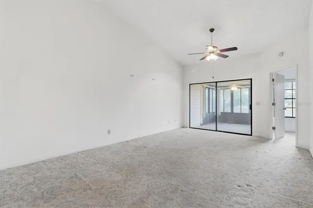 an empty room with chandelier fan and windows