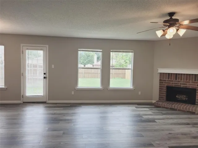 a view of an empty room with wooden floor fireplace and a window