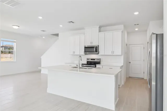 a kitchen that has a lot of white cabinets and stainless steel appliances