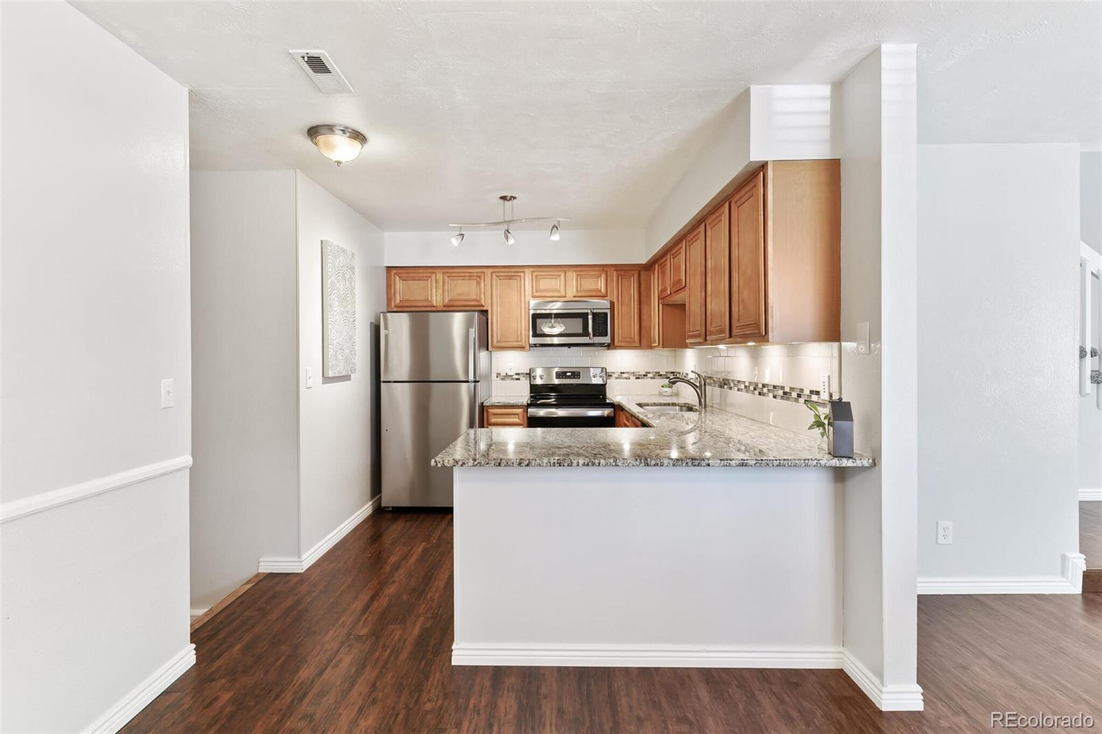 8417 Everett Way, Unit C Arvada, CO 80005 - Photo 15 of 34 a kitchen with stainless steel appliances granite countertop a refrigerator a stove top oven a sink and dishwasher with wooden floor