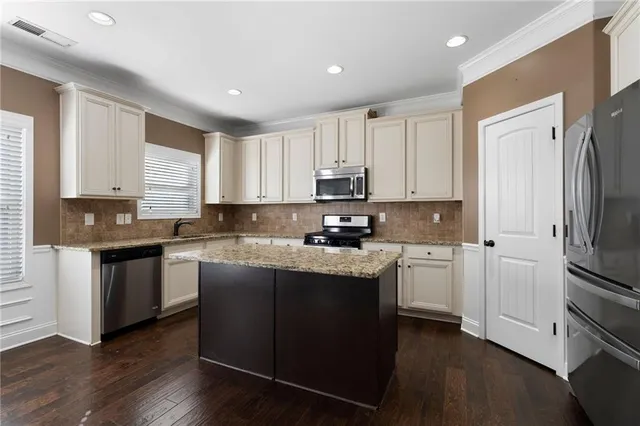 a kitchen with stainless steel appliances granite countertop a refrigerator a sink dishwasher a stove and white cabinets with wooden floor