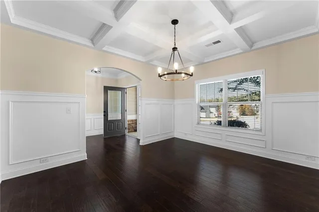 an empty room with wooden floor chandelier and windows