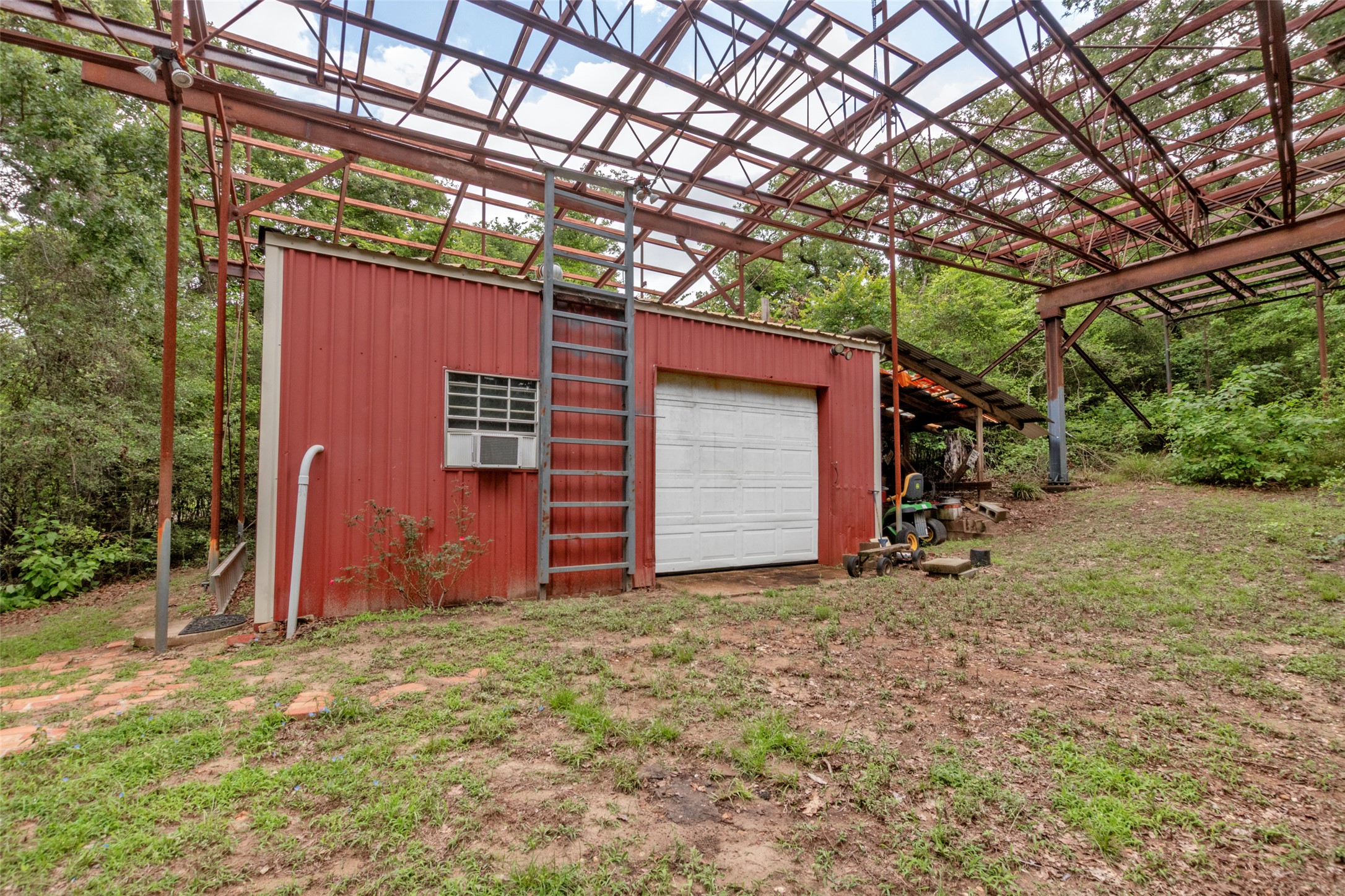 9997 Calhoun Road Bryan, TX 77808 - Photo 27 of 28 An expansive metal framework shelters a detached red outbuilding surrounded by mature trees.