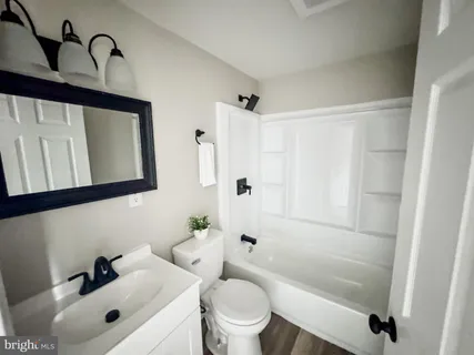 a bathroom with a bathtub shower sink vanity mirror and toilet