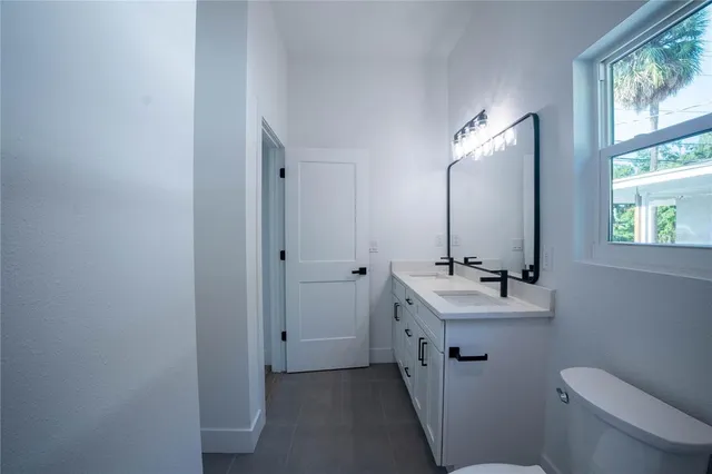 a bathroom with a toilet a sink a mirror a window and vanity