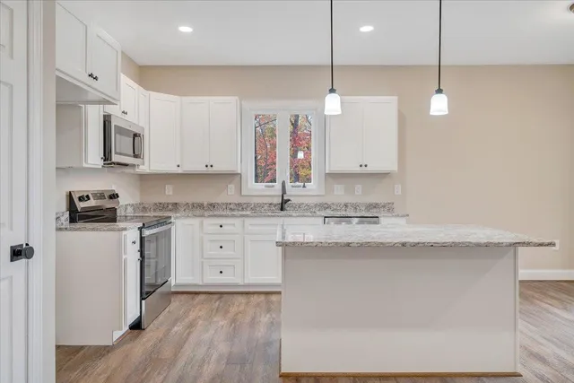 a kitchen with stainless steel appliances granite countertop a stove a sink and white cabinets with wooden floor