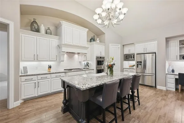 a kitchen with stainless steel appliances granite countertop a white refrigerator a sink dishwasher and white cabinets with wooden floor