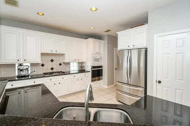 a kitchen with granite countertop a sink stainless steel appliances and white cabinets