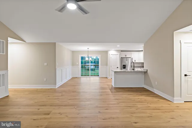 a view of kitchen and empty room with wooden floor and fan